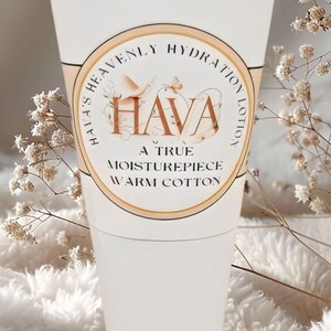 Puede incluir: Un tubo de loción blanco con base de madera. La etiqueta dice "HAVA Heavenly Hydration Lotion" con el texto "A True Moisturepiece Warm Cotton". El fondo es una textura suave, blanca y esponjosa con ramitas de flores secas.
