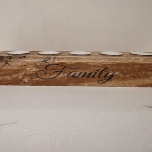 May include: A wooden candle holder with spaces for five tea lights. The word "Family" is carved into the wood. The wood has a natural, rustic appearance with visible grain and knots.