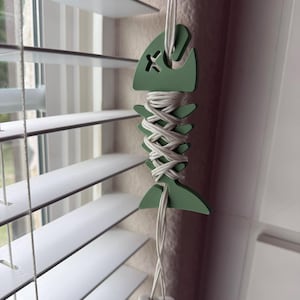 May include: A green wooden fish-shaped blind pull with white cord and two white tassel ends.