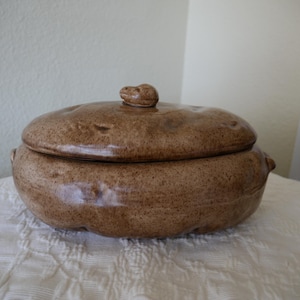 May include: A brown ceramic casserole dish shaped like a potato with a lid. The lid has a small potato-shaped knob.