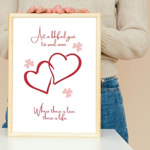 May include: A framed print with a white background and red hearts. The text in the image reads "At a bhfuil grá, tá saol ann." and "Where there is love, there is life."