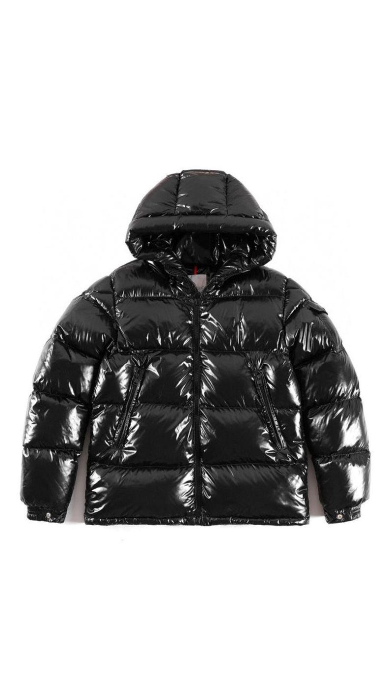 Op de afbeelding: Een glanzende zwarte pufferjas met capuchon. De jas heeft een glanzend, gewatteerd uiterlijk en een ritssluiting over de hele lengte. Hij heeft twee zijzakken en een kleine zak op de linkermouw. Deze winterjas is ontworpen voor warmte en stijl.
