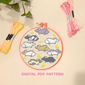 Op de afbeelding: Een borduurring met kruissteek met een patroon van verschillende gekleurde ratten en kaas. Roze, gele en oranje borduurgaren zijn rond de ring gerangschikt. De tekst "DIGITAL PDF PATTERN" staat onderaan.