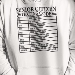 May include: White hoodie with a black graphic that says "Senior Citizen Texting Code" and lists common texting abbreviations and their meanings.