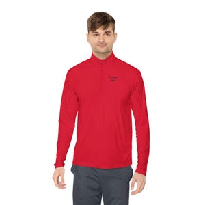 May include: A red long-sleeved top with a quarter-zip collar. The shirt features the text "Custom text" on the chest. The model is wearing grey trousers.