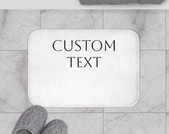 May include: White bath mat with black text that says "CUSTOM TEXT".
