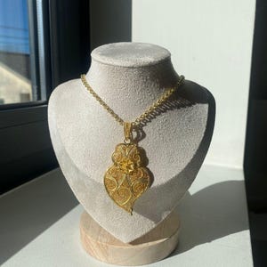 May include: A gold heart-shaped pendant necklace with intricate filigree details. The pendant is suspended from a delicate gold chain.