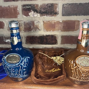 May include: Two ceramic bottles of Royal Salute Scotch whisky. The bottle on the left is blue with gold accents and the bottle on the right is brown with gold accents. Both bottles have a label with the words "Royal Salute" and "Scotch Whisky".