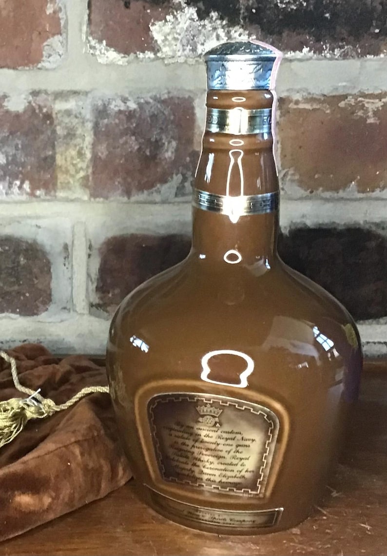 May include: A brown ceramic bottle with a silver top and a label that reads "By Royal Command, Supplying the Royal Navy,  is making annually one gift,  the presentation of the  'Chivas Regal'  to the  'Royal Navy'  in commemoration of her  Majesty the Queen's  Golden Jubilee, 1977."
