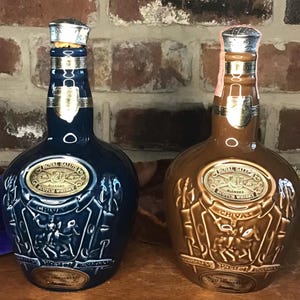 May include: Two ceramic bottles of Royal Salute 21 Year Old Blended Scotch Whisky. The bottle on the left is blue with a gold label and the bottle on the right is brown with a gold label.