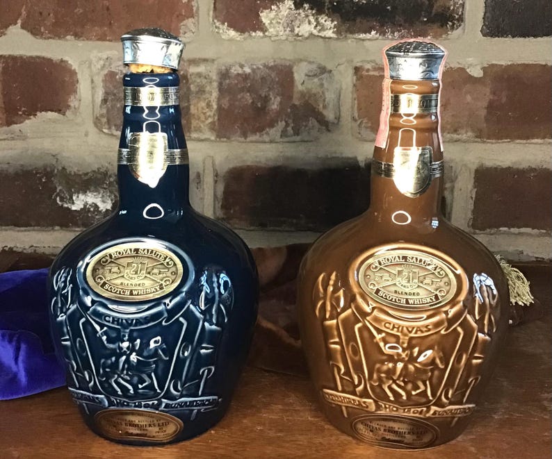 May include: Two ceramic bottles of Royal Salute 21 Year Old Blended Scotch Whisky. The bottle on the left is blue with a gold label and the bottle on the right is brown with a gold label.