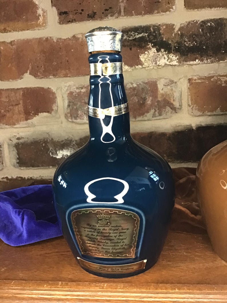 May include: A blue ceramic bottle of Chivas Regal Scotch Whisky with a gold label and a silver cap. The label reads "By an ancient custom, recognizing the Royal Navy, a whisky of beauty and rare quality in the prerogative of the Sovereign. This bottle of Chivas Regal Whisky created in the 1980s for the 125th Anniversary of the Royal Navy, is presented to Her Majesty Queen Elizabeth II."
