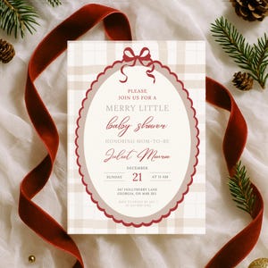 May include: A baby shower invitation with a cream and tan plaid background. The invitation has a burgundy scalloped oval frame with the text "MERRY LITTLE baby shower" and details for the event. A burgundy ribbon and pine sprigs decorate the scene.