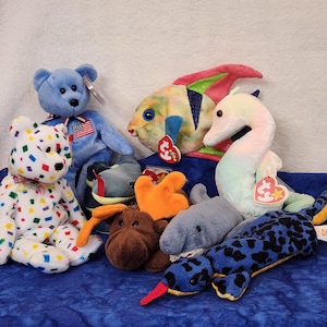 May include: A collection of colorful plush toys, including a blue bear, a white bear with colorful squares, a brown moose, a blue and white fish, a blue and yellow seahorse, and a blue and black snake.