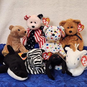 May include: A collection of seven colorful beanie baby plush toys, including a brown bear, a zebra, a unicorn, a black and white spotted dog, a black and white whale, a brown bear, and a red, white, and blue bear. Each toy has a Ty tag attached.