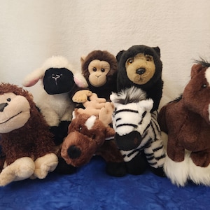 May include: A collection of plush animal toys, including a monkey, sheep, bear, zebra, and horse. The stuffed animals are various colors, with detailed features and soft textures. They are arranged on a blue surface.