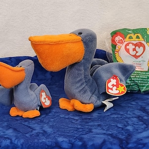 May include: Two blue and orange plush pelican beanie babies. The larger pelican has a tag that reads "Ty Scoop, Toy Animal, Not for resale, Distributed exclusively by McDonald's, Ty Inc."