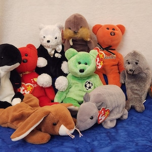 May include: A collection of nine colorful beanie baby plush toys, including a black and white orca, a red and white bear, a white bear wearing a tuxedo, a brown walrus, an orange bear, a green bear, a gray seal, a brown rabbit, and a gray armadillo.