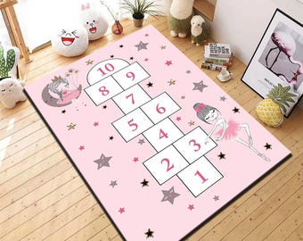 May include: Pink hopscotch rug with a ballerina illustration and star accents. The rug features numbered squares for playing hopscotch, with a ballerina on the side. The rug is designed for children's playrooms.