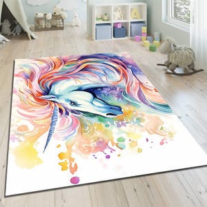Può includere: Tappeto rettangolare con un'illustrazione ad acquerello di un unicorno. L'unicorno ha un corpo bianco, un corno blu e una criniera fluente in tonalità di rosa, viola e arancione. Il tappeto ha uno sfondo bianco con schizzi di vernice colorati.