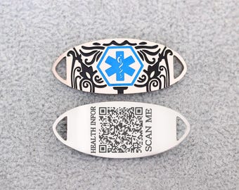 May include: Two silver-colored medical alert tags. One tag features a blue medical symbol within a black decorative border. The other tag has a QR code and the text "HEALTH INFOR SCAN ME".