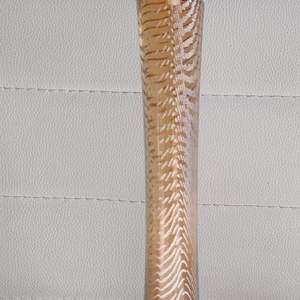 May include: A tall, slender perfume bottle with a light brown liquid inside. The bottle has a silver neck and a pink, rounded cap. The glass is decorated with a white, zebra-like pattern. The brand name is visible on the bottle.