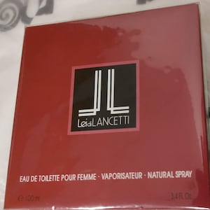 Pode incluir: Uma caixa vermelha de Eau de Toilette Leidi Lancetti para mulheres. A caixa apresenta um quadrado preto com as letras "JL" em branco e o nome da marca. A caixa contém 100 ml de perfume.