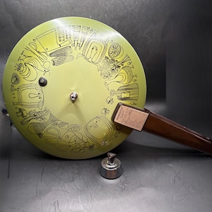 May include: A vintage avocado green Presto pressure cooker lid with a brown handle and a silver pressure regulator. The lid features black line art of kitchen utensils and food items. The product label reads "Presto Deluxe".