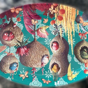 Puede incluir: Plato decorativo ovalado con un fondo turquesa que presenta ilustraciones de pájaros, nidos, mariposas y flores. Los nidos son marrones y contienen pájaros coloridos. Las mariposas son naranjas y las flores son rojas.