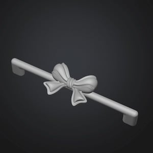 May include: A light gray cabinet pull with a bow design in the center. The pull is a straight bar with curved ends. The bow is detailed with rounded edges and a knot in the center. The background is a dark gray.