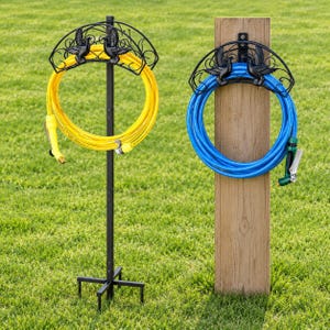 May include: Two black metal hose hangers featuring decorative bird silhouettes. One hanger is mounted on a vertical black metal stand holding a yellow garden hose, while the other is attached to a wooden post holding a blue garden hose.