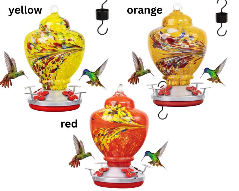 May include: Three glass hummingbird feeders with metal bases and red flower-shaped feeding ports. The feeders are labeled yellow, orange, and red, featuring swirling multi-colored patterns in the glass reservoirs and black metal hanging hooks.