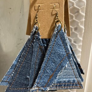 May include: A pair of denim triangle earrings with brown stitching and gold-toned hooks.
