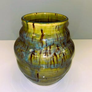 May include: A handmade ceramic vase with a unique, textured design. The vase features a blend of green, blue, and brown colors, with a glossy finish. The vase has a wide, rounded body and a slightly flared rim, perfect for displaying flowers or as a decorative piece.