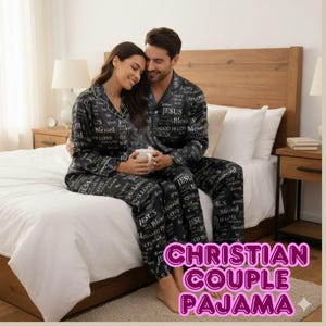 May include: A couple wearing matching black pajamas printed with religious words like "Jesus" and "Blessed." They are sitting on a bed, with the woman holding a white mug. The pajamas have a button-down shirt and pants design.