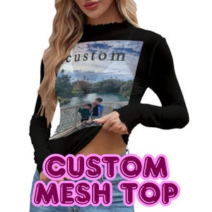 May include: Black long-sleeved mesh top with a high neckline. The top has a custom photo print on the front, with the word "custom" at the top. The bottom of the top has the words "CUSTOM MESH TOP" in a pink bubble font.