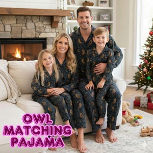 May include: A family of four wearing matching navy blue pyjamas with an owl and moon pattern. The pyjamas have a button-down top and trousers. The text "OWL MATCHING PAJAMA" is displayed in a pink font at the bottom of the image.