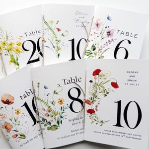 May include: White wedding table number cards with floral watercolor designs. Each card features a large black number, such as 2, 6, 8, or 10, and is tied with twine. Some cards include names and dates.