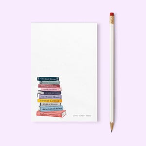 May include: A white notepad with a stack of colorful book illustrations and the text "JONES STREET PRESS". A pencil with a red eraser rests on the right side. The book titles include "The Great Grocery" and "Realistic Expectations".