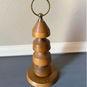 May include: A wooden decorative stand with a brass ring at the top. The stand has a stacked design with four tiers and a round base.