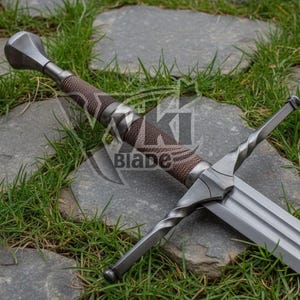 May include: A silver-colored sword with a brown, textured handle and a double-edged blade. The sword is lying on a stone surface with green grass around it. The handle has a diamond pattern. The word "Blade" is visible on the image.
