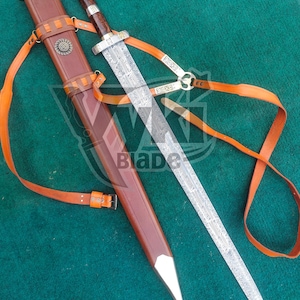 May include: A detailed image of a sword with a brown leather sheath and orange straps. The sword has an ornate silver handle and a blade with intricate etched designs. The sheath has a decorative metal emblem. The word "Blade" is visible on the image.