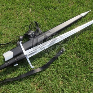 May include: A long, silver sword with a cross-shaped hilt and a black leather-wrapped handle rests on green grass. A black leather sheath and belt are next to the sword. The sword's blade is long and sharp.