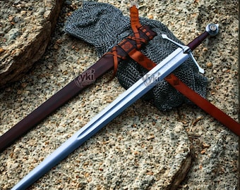 May include: A silver sword with a brown handle and crossguard, lying on a stone surface. The sword has a long, sharp blade and is accompanied by a brown leather sheath and chainmail. The image includes the text "yki blade".