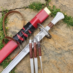 May include: A silver-toned sword with a dark wood handle and a metal crossguard, accompanied by a red scabbard featuring black leather wrapping and a brown leather strap. Three small, matching knives with wooden handles are positioned in front.