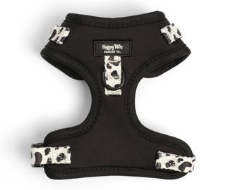 May include: Black dog harness with a white and black leopard print trim. The harness has a metal D-ring and a label that reads "Happy Tails Harness Co."