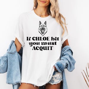 Puede incluir: Camiseta blanca con una ilustración en blanco y negro de un pastor alemán y el texto "If CHLOE bit you must ACQUIT".
