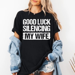 May include: Black t-shirt with white text that reads "Good Luck Silencing My Wife".