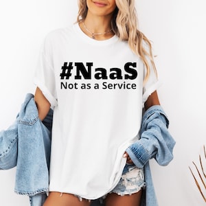 以下が含まれることがあります： 黒い文字で「#NaaS Not as a Service」と書かれた白いTシャツ。青いデニムジャケットとデニムショーツを着用しています。モデルはネックレスをしています。