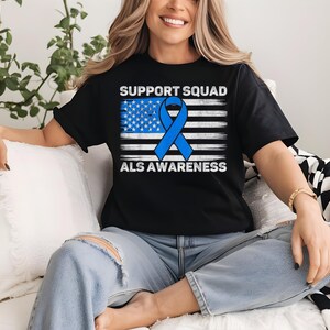 May include: A black t-shirt with a blue ribbon and an American flag design. The text "Support Squad ALS Awareness" is printed on the shirt.
